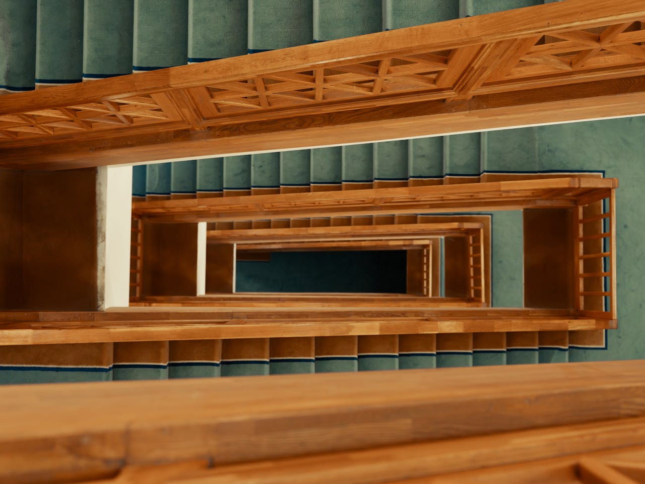 An intriguing view of a wooden staircase with teal carpet, captured from above, showcasing geometric symmetry.